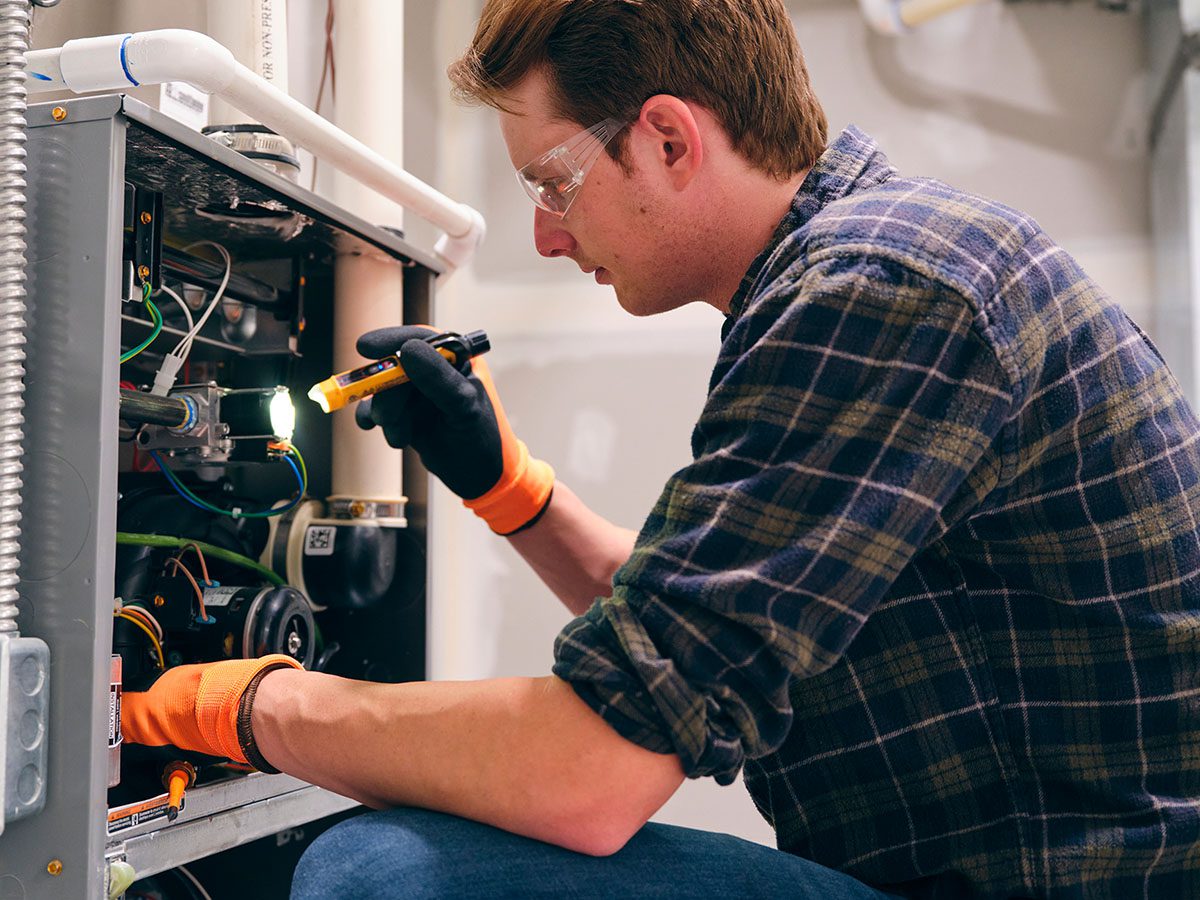 Man wearing safety glasses, holding a flashlight, and looking into a furnace.