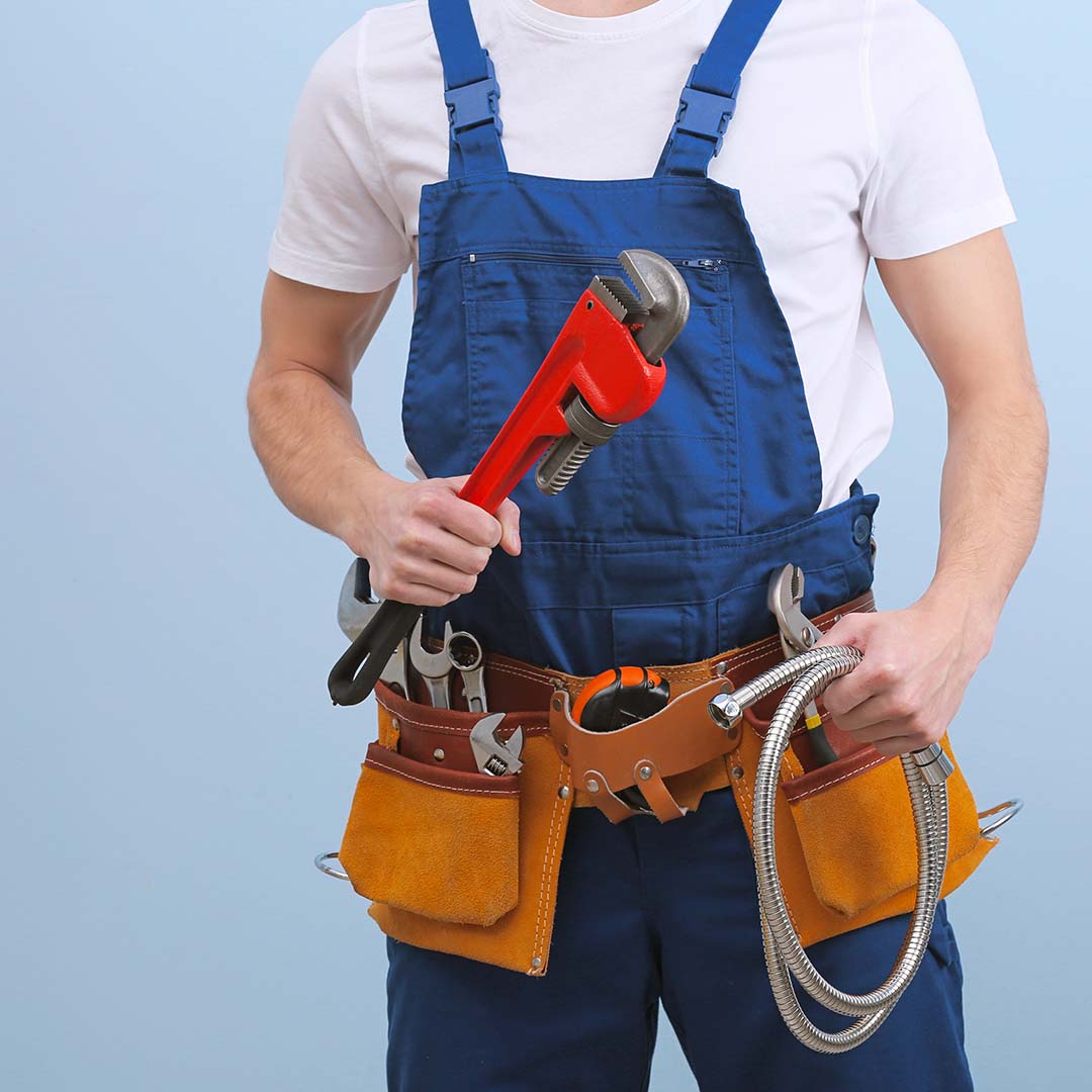 1080x1080Social-4-615e106b584da An image of a plumber holding a wrench and wearing a tool belt.